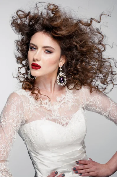 Vacker ung kvinna med långa bruna hår, röda läppar, smycken i brudklänning modell ganska poser på studio. — Stockfoto