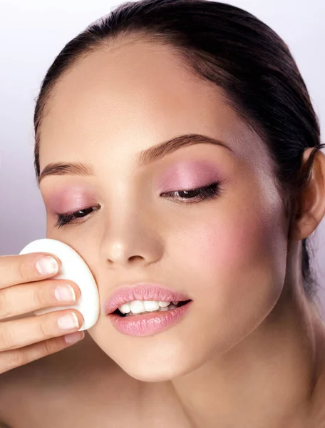 Femme appliquant de la poudre sèche à l'aide d'un coussin cosmétique sur sa peau faciale. Photo d'une jolie fille avec un maquillage parfait sur fond beige. Concept de beauté Image En Vente