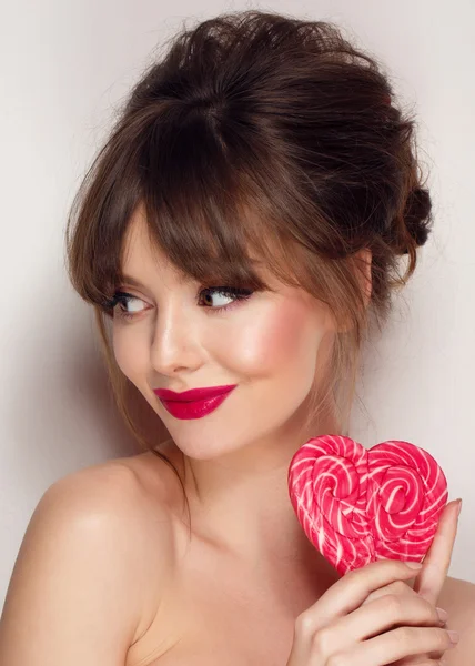 Mode makeup. Skönhet flicka stående håller färgglada lollipop. Varma röda läppar. — Stockfoto