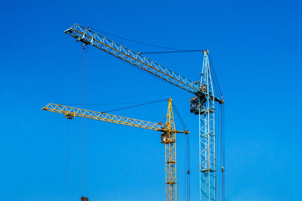 Two cranes against the blue sky. Blue and yellow crane at the construction site.