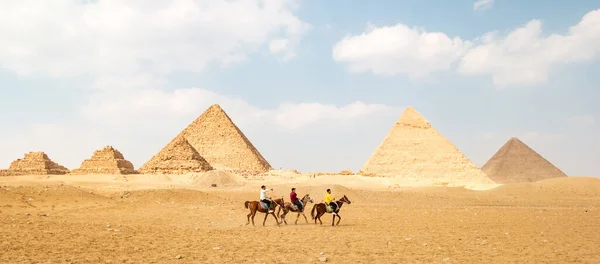 Giza 'daki Büyük Mısır piramitlerinin panoramik görüntüsü ve önlerinde üç süvari.