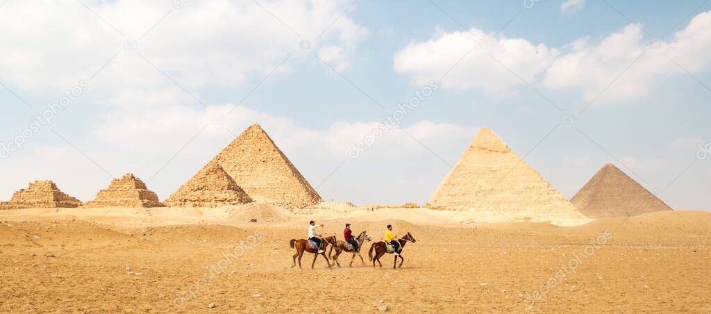 Panoramic view of Great Egyptian pyramids in Giza and three riders in front of them.