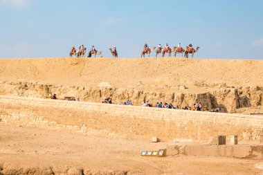 Giza, Mısır - Şubat 2021: Mısır piramitleri yakınında yürüyen turistli deve kervanı.