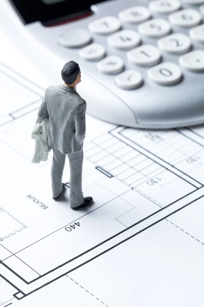 Homme d'affaires miniature avec calculatrice sur plan de l'architecte pour le coût du logement — Photo