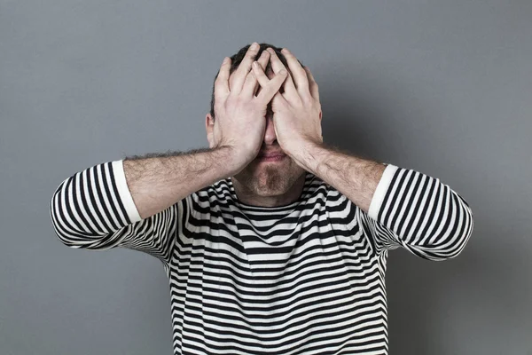 Disturbed man with striped sweater hiding face for blindness expressing regret — Stock Photo, Image