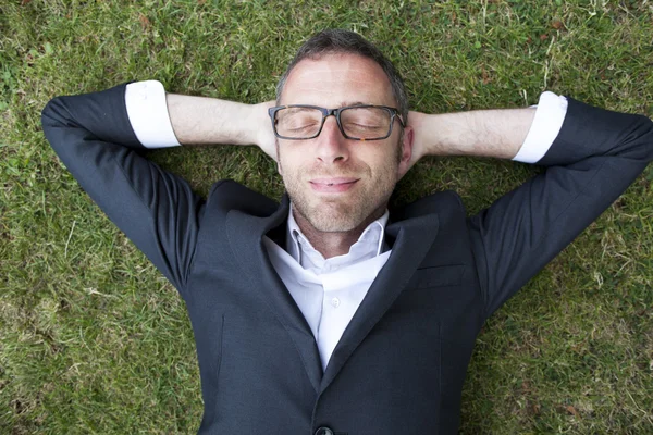 Thrilled relaxed businessman lying on grass outdoors — Stock Photo, Image