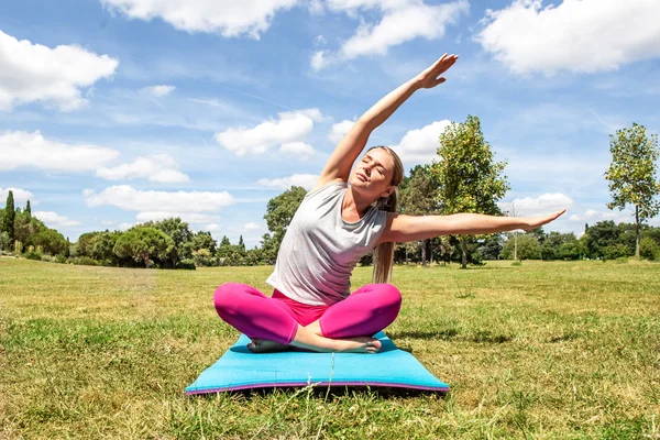 Rilassato giovane donna bionda che fa yoga con piegato parte superiore del corpo sul tappeto esercizio sopra cielo blu estate — Foto Stock