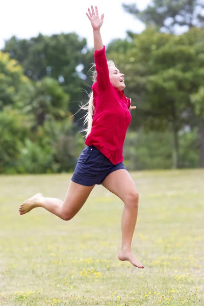 Усміхнена красива молода жінка стрибає високо для відпочинку в зеленому парку — стокове фото