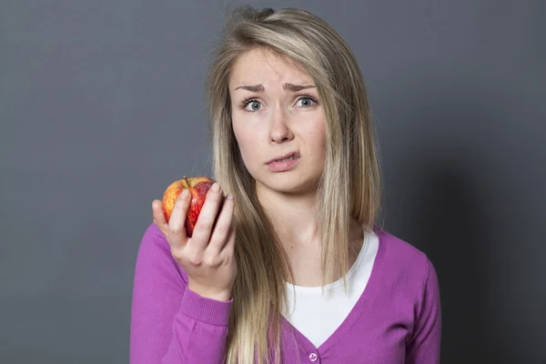 Symbol för matkoncept-olycklig 20s blond kvinna ogillar smaken av ett rött äpple — Stockfoto