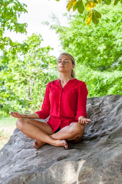 All'aperto relax respirando ragazza bionda meditando sotto un albero su una pietra — Foto Stock