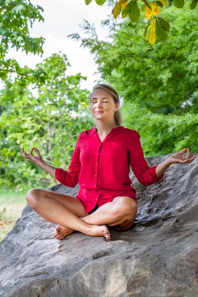 Felice ragazza bionda meditando sotto un albero su una pietra — Foto Stock