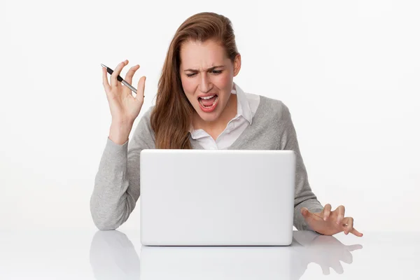 Enraged 20s woman writing on laptop on sparse white desk — Stock Photo, Image