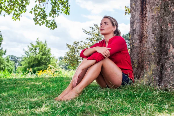 Thinking young woman sitting under a tree for summer freshness — Stock Photo, Image