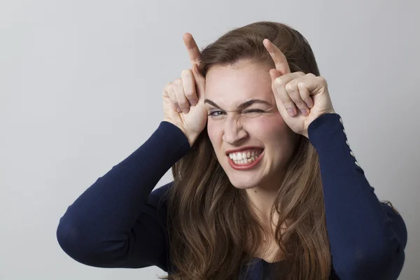 Zwinkernde junge Frau mit Doppelfingerhörnern für freches Zeichen — Stockfoto