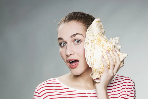 Amazed gorgeous young woman with shell to her ear for exotic vacation — Stockfoto
