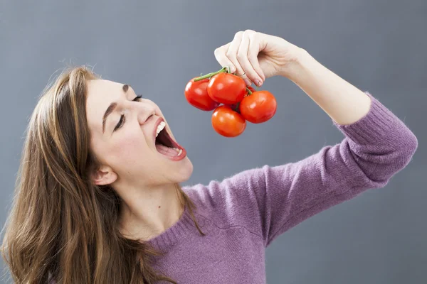 Beautiful 20s girl eating tomatoes with appetite for vitamins and appetizing food — Stockfoto