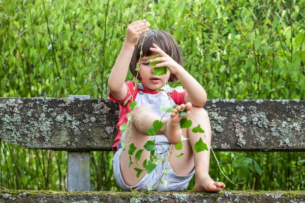 Bahçede doğayı öğrenmek için sarmaşık yaprakları ile oynayan çocuk — Stok fotoğraf