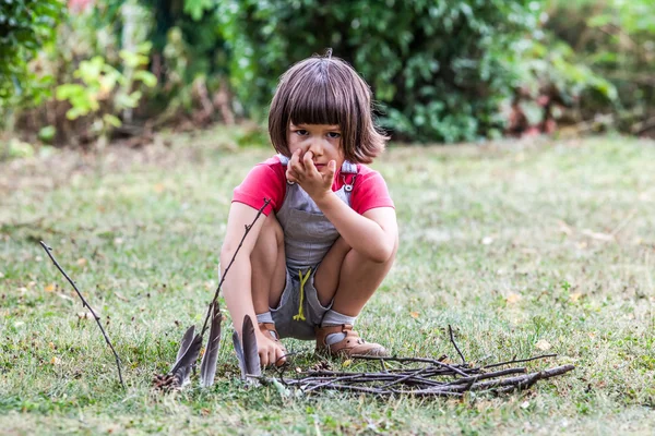 Думаючи, маленька дитина грає з дерев'яними паличками в зеленому парку — стокове фото