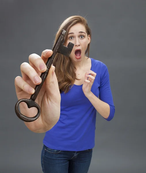 Sorpresa giovane donna mostrando una grande chiave per simbolo spaventoso — Foto Stock