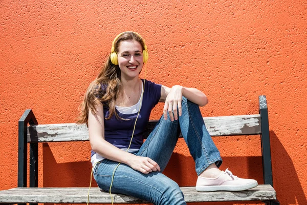 Χαμογελαστός θηλυκός έφηβος ακούγοντας μουσική στα πολύχρωμα ακουστικά της — Φωτογραφία Αρχείου