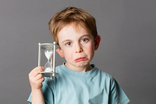 Worried young child with pouting mouth holding an egg timer — Stock fotografie