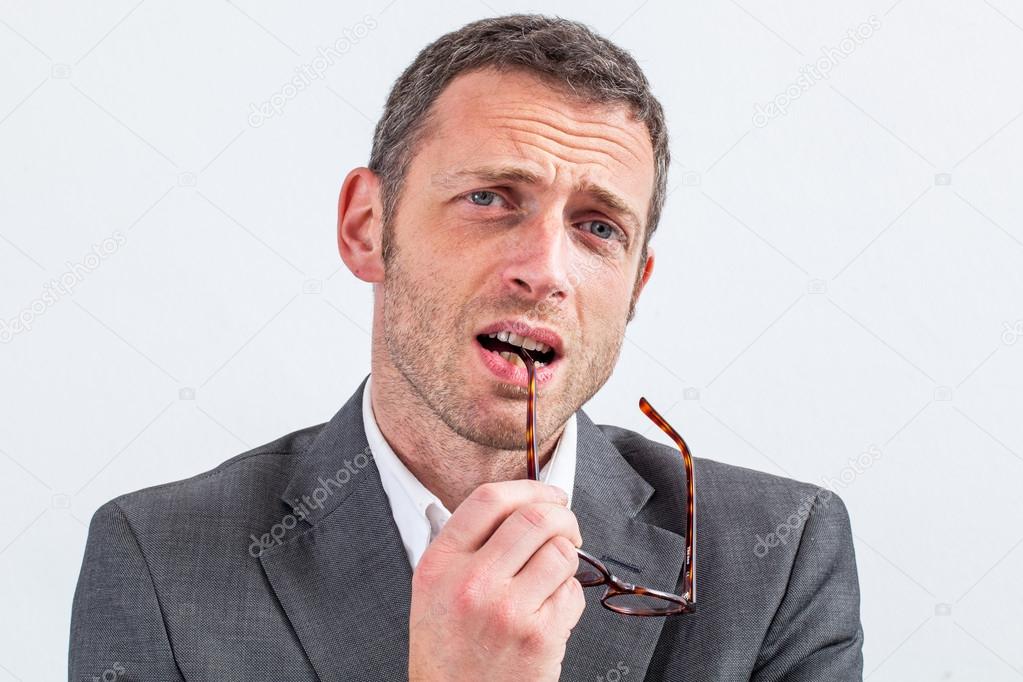 thinking middle aged businessman biting his eyeglasses expressing doubt
