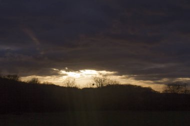 Yoğun kara kümülüs bulutları parlak bir günbatımını kaplıyor ilham verici bir kış için zıt ışık