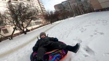 Mutlu kış aile aktiviteleri. Bir baba altı yaşındaki oğlunu kış boyunca şişme bir kar tüpüne sokuyor. Çocuk güler ve gezintiden zevk alır, sonra neşeyle tünelden karın içine düşer, neşeli ve enerjik bir an yaratır.