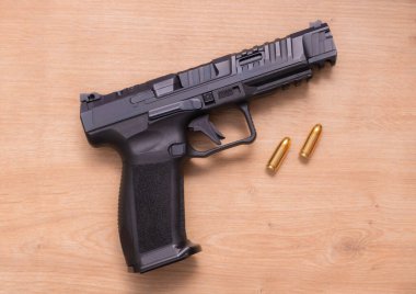 A modern semi-automatic pistol top view on a wooden surface next to two golden bullets. The sleek design and metallic finish highlight its advanced engineering.