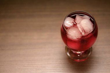 Chilled red beverage in glass with ice cubes. The condensation on the glass and the clarity of the ice create a visually appealing and inviting image. Selective focus.