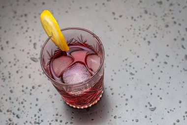 Refreshing red cocktail with ice and lemon garnish. A close-up of a refreshing red cocktail served in a vintage crystal glass. Selective focus.