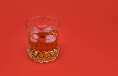 Isolated crystal glass filled with whiskey and ice cubes on red background. Object for themes related to luxury, nightlife and celebration.