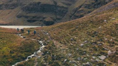 Dağ yürüyüşçüleri dalgalı dereyi, çimli yamaçları ve kayalık yolları, öncü grup sırt çantalarını, havadan çekimleri