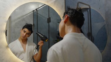 Genç bir adam banyoda saç kurutma makinesi kullanıyor..