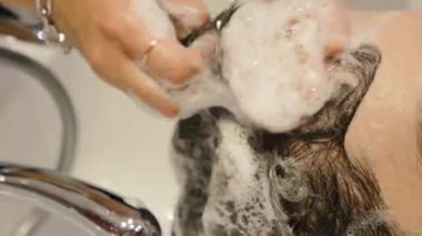 Erkek müşterinin saçını yıkarken köpük çıkaran profesyonel stilist..