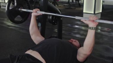 Vücut geliştirici antrenman sırasında bir bankta uzanırken halteri kaldırıyor..