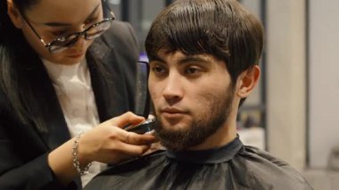 Modern berber dükkanında erkek sakalını şekillendirmek için budayıcı kullanıyor..