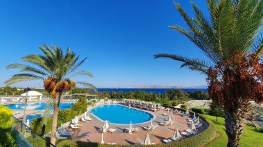 Kos, Yunanistan - 15 Eylül 2019: Salgının etkileri. Güneşli bir günde palmiye ağaçlarının altında boş güneşlenirler ve yüzme havuzları.