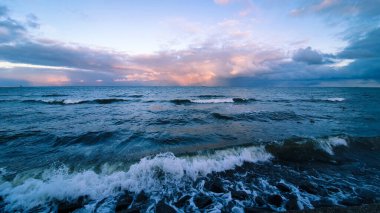 Dalgalı deniz ve batan güneşin renklerinde gökyüzü