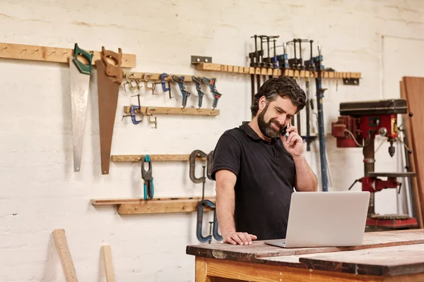 Kézműves beszél telefonon, és nézi laptop — Stock Fotó