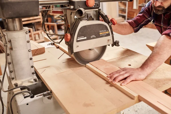 Carpenter cutting piece of wood with saw — Stock Photo, Image