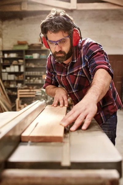 Carpenter cutting wooden plank with saw — Stock Photo, Image