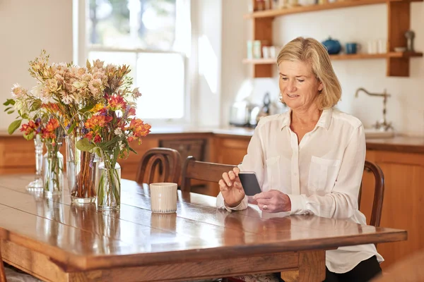 Woman reading message on phone in kitchen — ストック写真