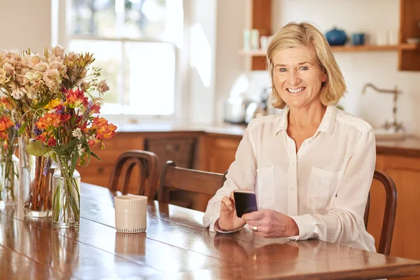 Woman reading message on phone in kitchen — ストック写真