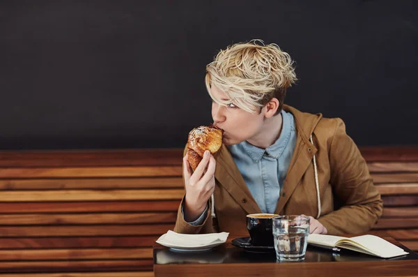 Женщина откусывает круассан в кафе — стоковое фото