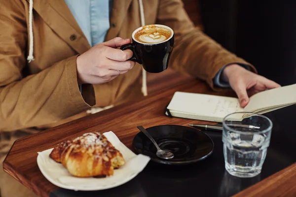 Γυναίκα με cappucino και σημειωματάριο στο μοντέρνο καφέ — Φωτογραφία Αρχείου