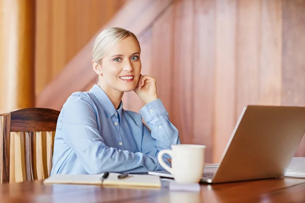 Affärskvinna vid skrivbord tittar och ler i kameran — Stockfoto