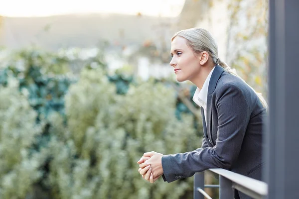 Businesswoman leaning against railing of balcony — Stock Photo, Image