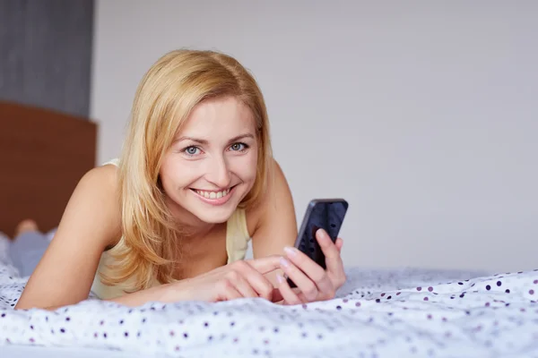 Kobieta za pomocą telefonów komórkowych w łóżku — Zdjęcie stockowe