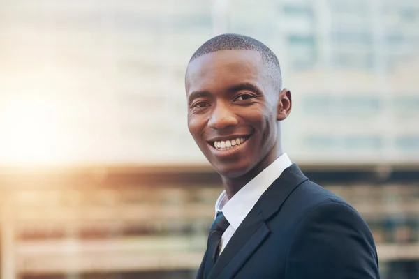 Hombre de negocios sonriendo a la cámara con edificios borrosos — Foto de Stock